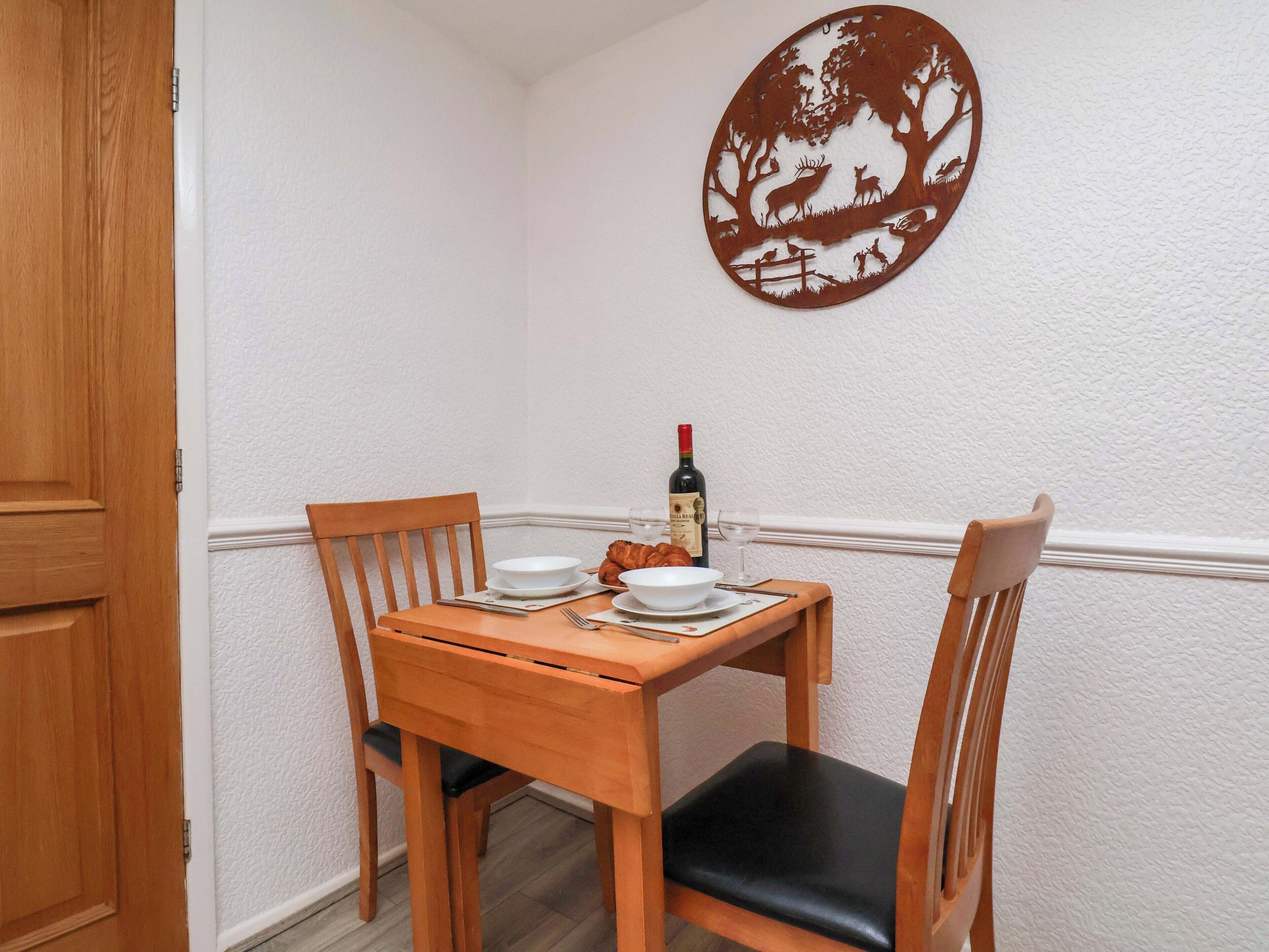 Zona pranzo con tavolo in legno, due sedie, una bottiglia di vino e una decorazione a parete.