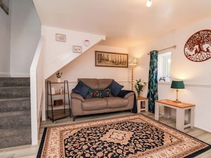 A living room with a sofa, a patterned rug, a lamp, a painting, and a staircase.