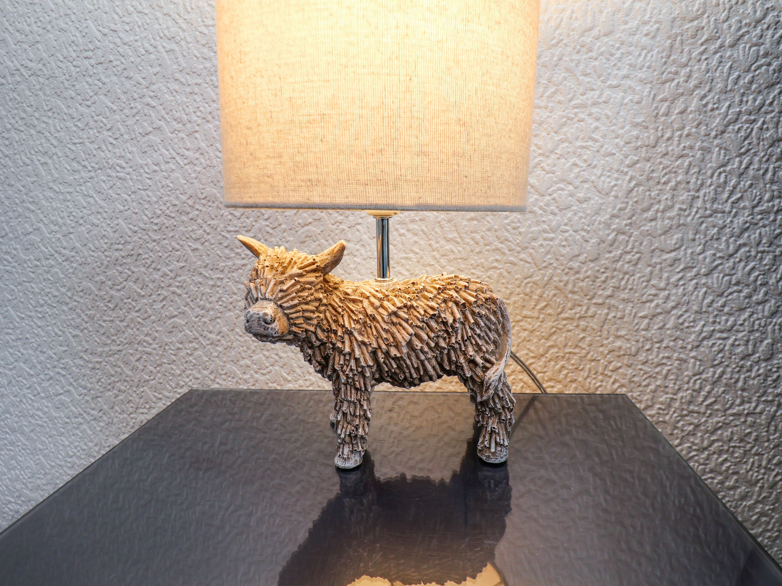 Pared con textura y una lámpara con una figura decorativa de animal sobre una superficie oscura.