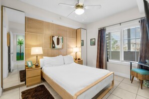 A bedroom with a large bed, wooden headboard, two bedside tables with lamps, a nightstand with a framed photo, a window with curtains, and a ceiling fan. - Cassine Station by Panhandle Getaways (Santa Rosa Beach)
