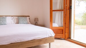 A bedroom with a wooden bed, a nightstand, a lamp, and a sliding glass door to a balcony. - Sardinia Re - Villa Green Val (Alghero)