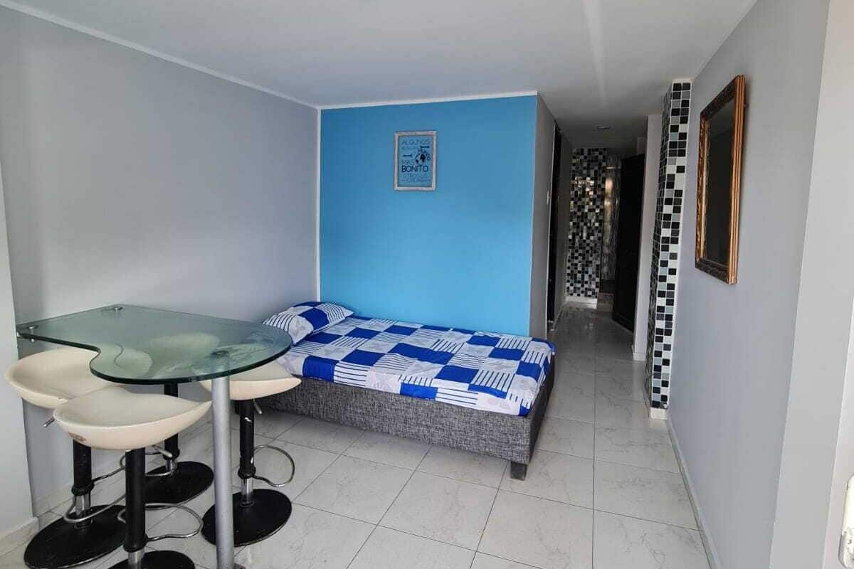 A small, modern room with a bed, a glass table with two chairs, and a tiled floor.