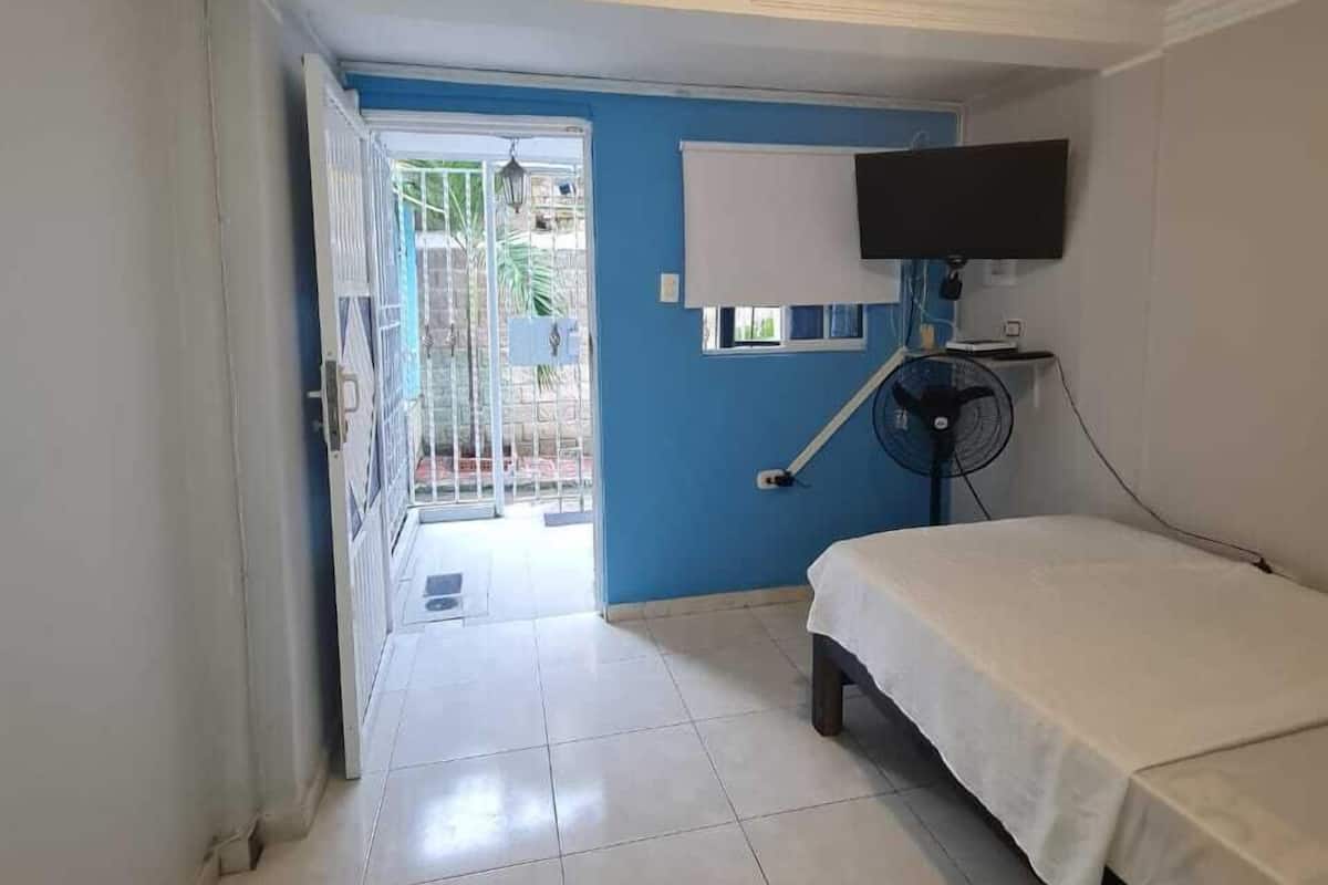 A room with a bed, a TV mounted on the wall, a ceiling light, and a fan.
