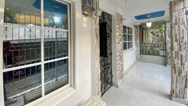 A hallway with white walls, a blue ceiling, and a tiled floor. There are windows with metal bars and a door with a black metal gate. - Casa Turística los Doce Apostoles  (Cartagena)