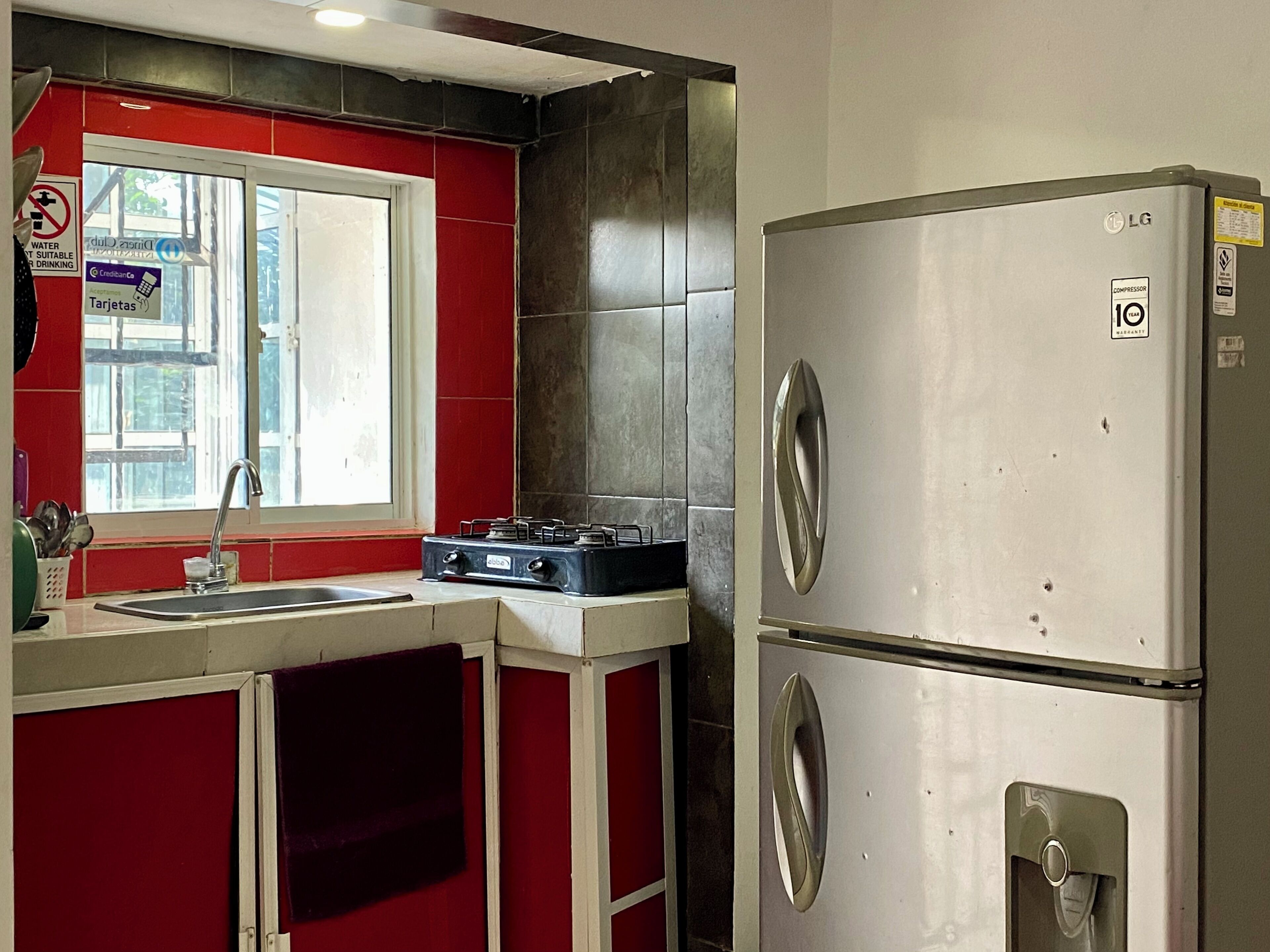 Una cocina compacta con estufa a gas, un refrigerador de acero inoxidable y una ventana con vista a la calle.