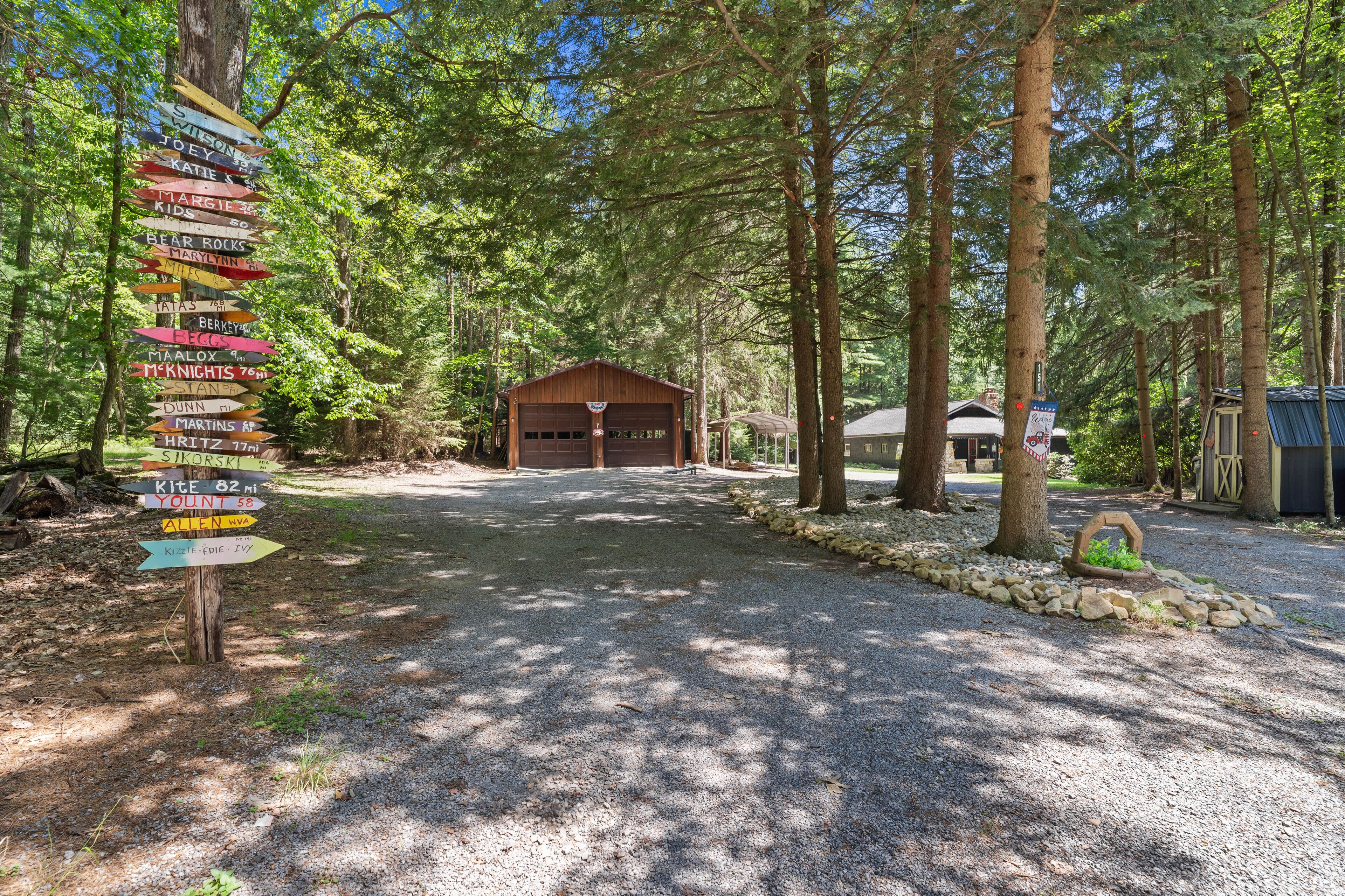 Un chemin de gravier mène à un chalet en bois doté d’un garage, le tout étant entouré de grands arbres.