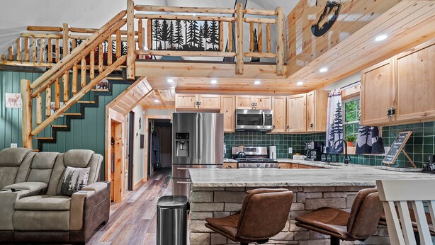 A modern kitchen with wooden cabinets, a stainless steel refrigerator, and a stone island with bar stools. - Northwoods Ln Cabin in Clear Creek by Tranquility Retreats (Sigel)
