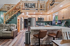 A modern kitchen with wooden cabinets, a stainless steel refrigerator, and a stone island with bar stools.