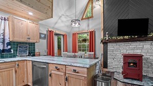 A modern kitchen with wooden cabinets, a built-in dishwasher, and a stone fireplace. - Northwoods Ln Cabin in Clear Creek by Tranquility Retreats (Sigel)