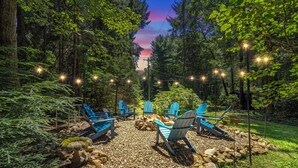 A forested area with outdoor seating and a fire pit. - Northwoods Ln Cabin in Clear Creek by Tranquility Retreats (Sigel)