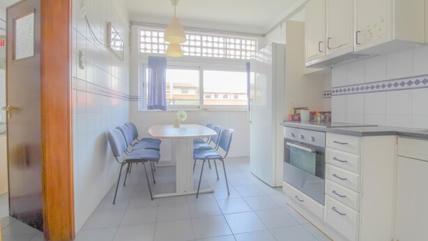 Een keuken met witte kasten, een fornuis en een eettafel met stoelen.