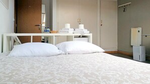 Een slaapkamer met een bed, een kledingkast en een klein tafeltje met handdoeken en toiletartikelen.