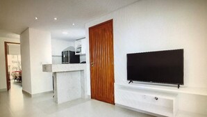 Un soggiorno moderno con una TV a schermo piatto montata a parete, una porta in legno e un angolo cucina sullo sfondo.