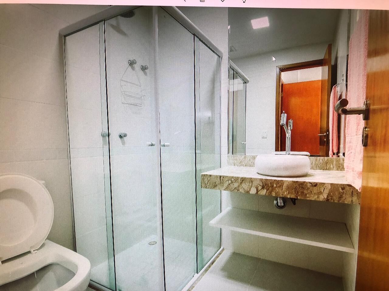 Ein Badezimmer mit einer Duschkabine aus Glas, einer weißen Toilette und einer Marmorplatte mit Waschbecken.