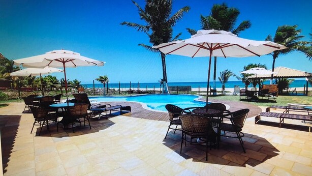 Zona piscina con sedie a sdraio e ombrelloni, vista libera sull'oceano e una piscina.