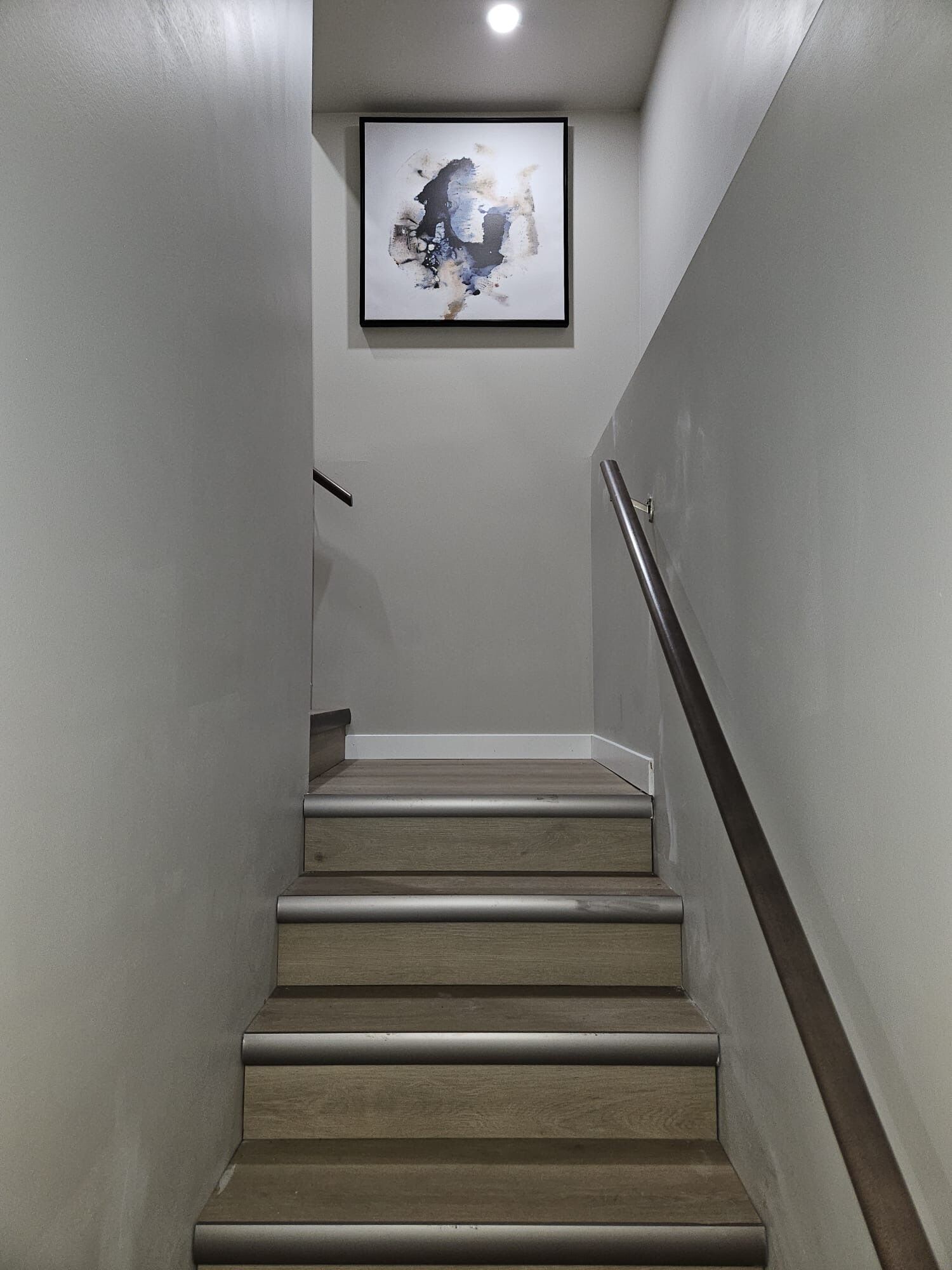 A staircase with wooden steps and a metal handrail, leading to a landing with a framed abstract artwork.
