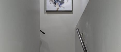 A staircase with wooden steps and a metal handrail, leading to a landing with a framed abstract artwork.
