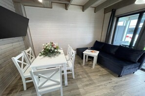Ein modernes Interieur mit einem weißen Esstisch, weißen Stühlen, einem dunklen Sofa und einem kleinen Beistelltisch.