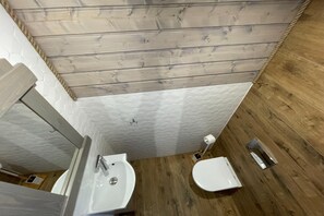 Ein Badezimmer mit Holzboden, weißen Wänden mit Struktur und einem Waschbecken sowie einer Toilette.