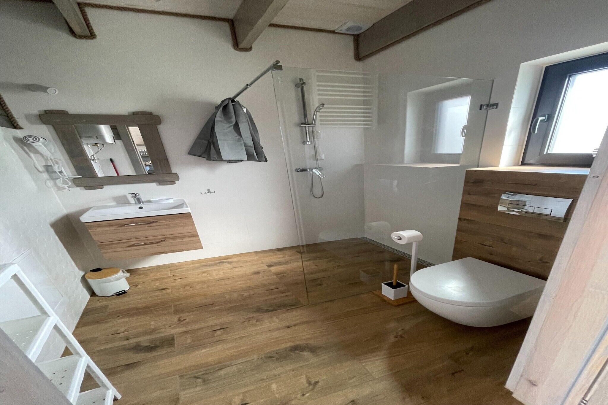A compact bathroom with a wooden floor, a white sink, a toilet, and a shower.