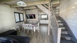 Ein gemütlicher Raum mit einer Holztreppe, einem Essbereich inklusive Tisch und Stühlen, einer Couch und einem an der Wand befestigten Fernseher.