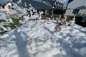 En gruppe mennesker leger med skum i et udendørs område med huse i baggrunden.
