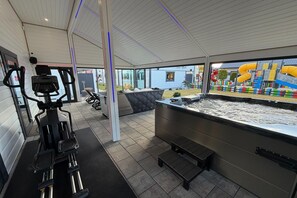 Ein Fitnessraum mit Trainingsgeräten, einer Whirlwanne und Blick auf einen Spielplatz.