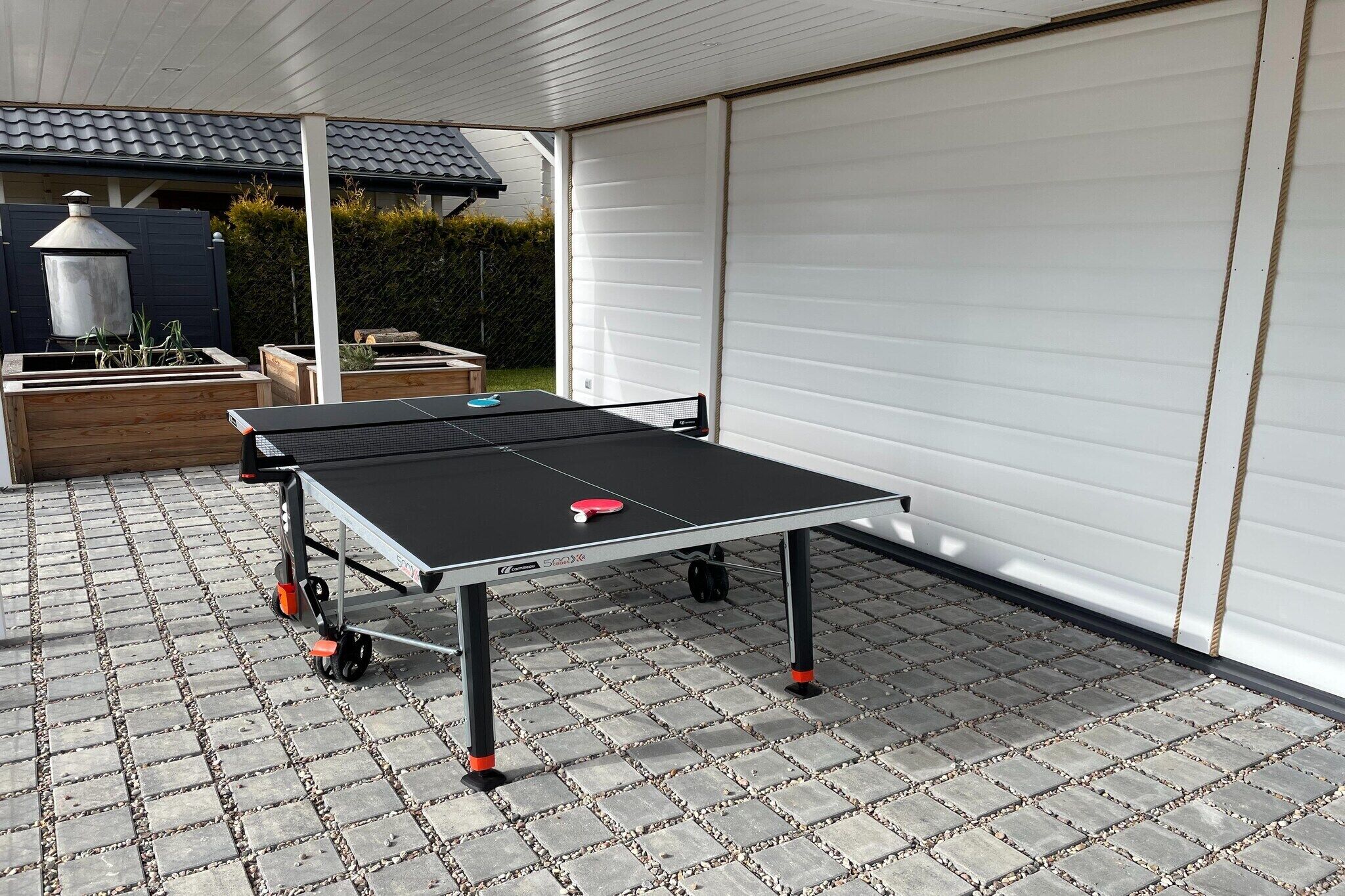 Une table de ping-pong sur une terrasse dallée, avec une porte de garage en arrière-plan.