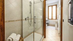 A modern bathroom with a glass-enclosed shower, a wooden-framed door leading to a bathroom with a sink and mirror. - Emilia Studios 1 (Modena)