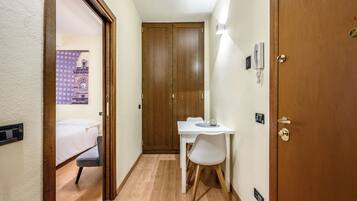 Quarto de hotel com cama, escrivaninha com cadeira, guarda-roupa de madeira e telefone fixado na parede.