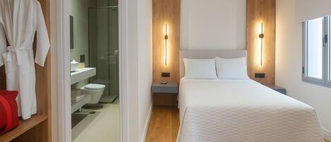 A modern bedroom with a large bed, bedside tables, a wardrobe, and a bathroom visible through an open door.
