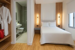 Quarto moderno com uma cama grande, mesas de cabeceira, um guarda-roupa e um banheiro visível por uma porta aberta.