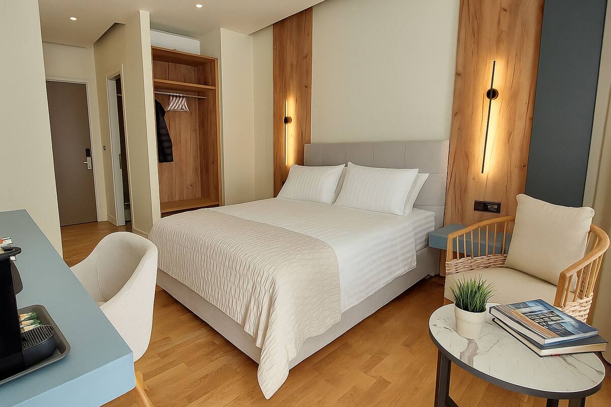 Una habitación de hotel moderna con una cama grande, una zona de estar con una silla y una mesita, y un armario.