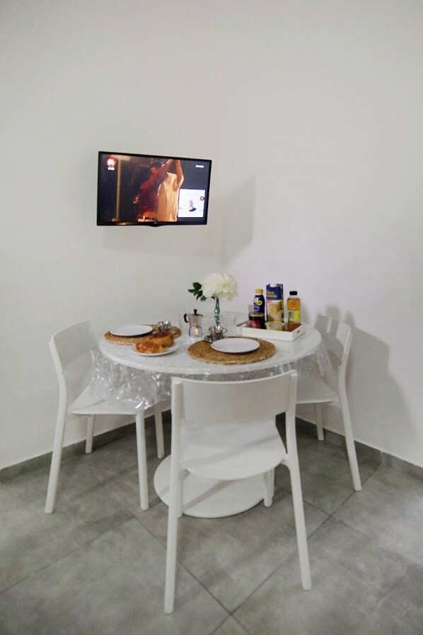 A dining area with a table set for two, a television mounted on the wall, and various food items and condiments on the table.