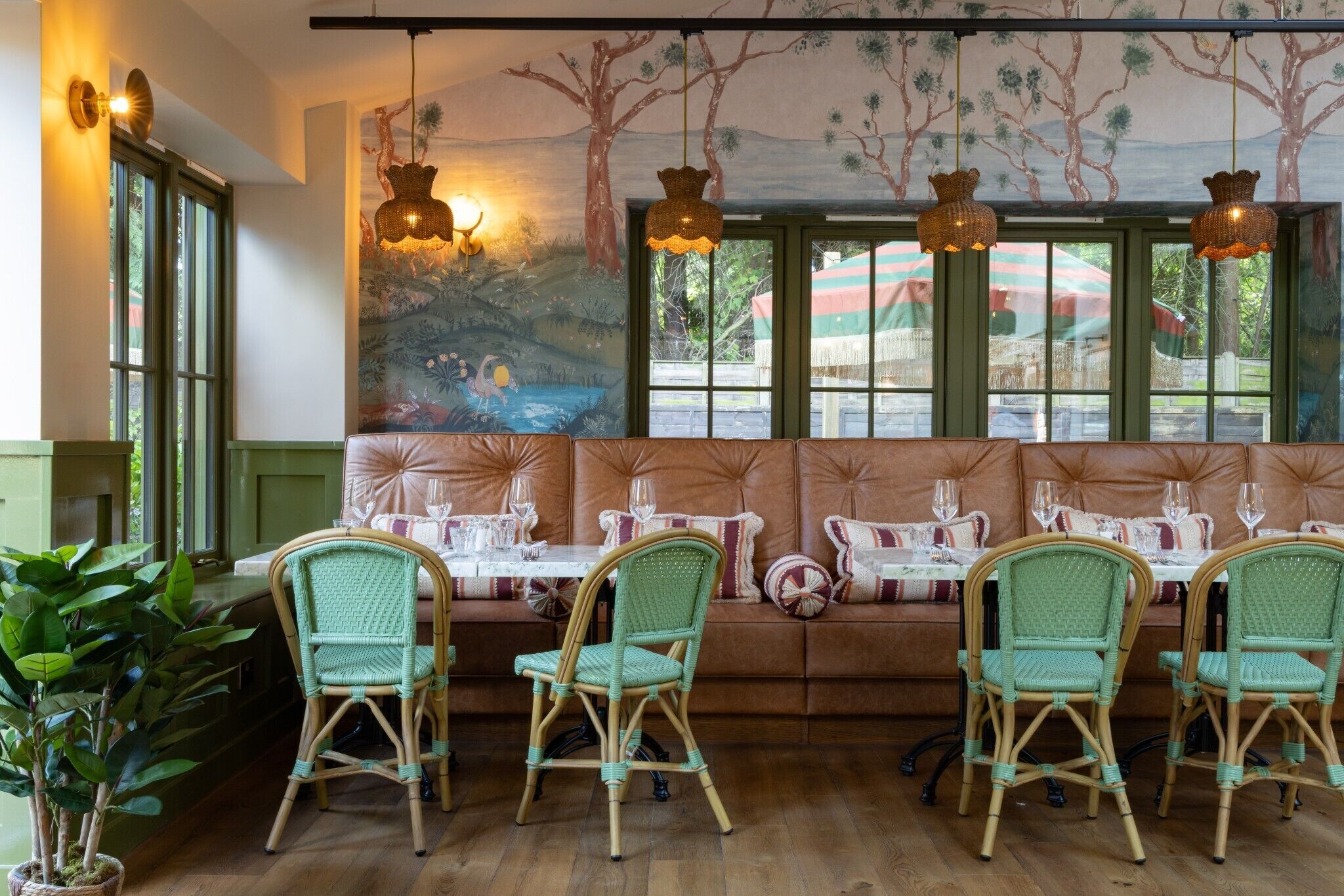 A restaurant with wicker chairs, a cushioned bench, and a mural on the wall.