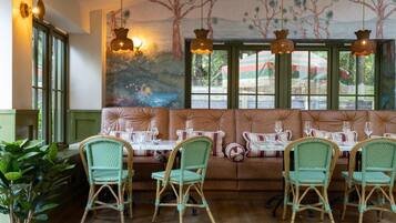 A restaurant with wicker chairs, a cushioned bench, and a mural on the wall.