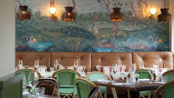 Un comedor con sillas de mimbre, un mural de una escena de bosque y lámparas colgantes de mimbre.