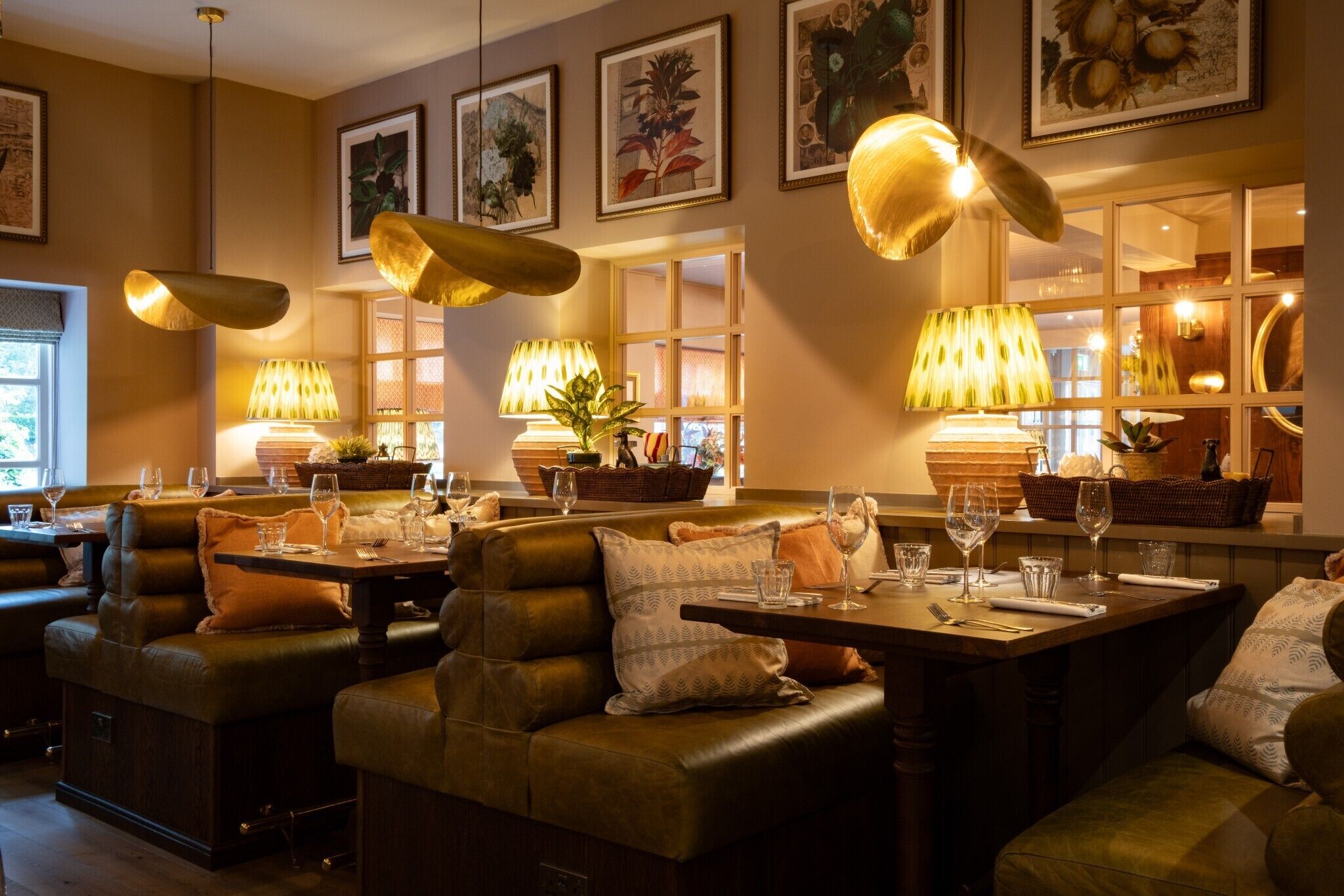 A restaurant with leather booths, table settings, and hanging lamps.