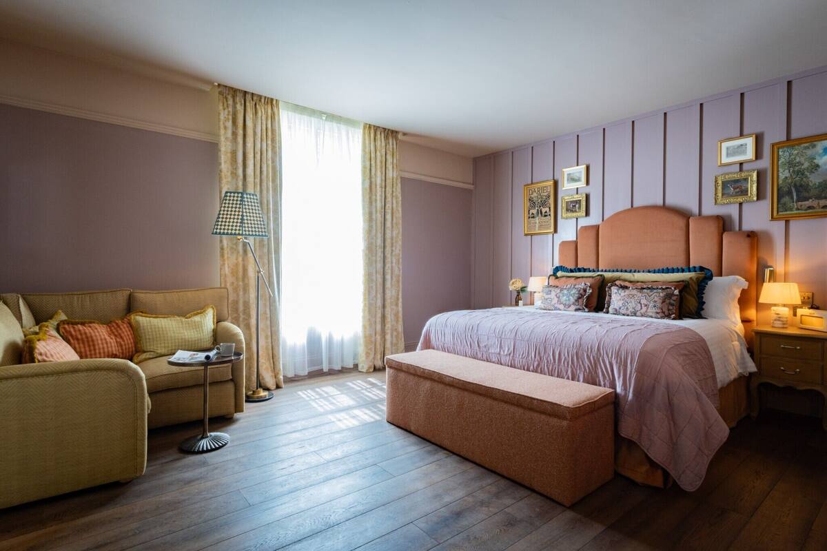 Un dormitorio con cama, sofá, mesita de noche, lámpara y ventana con cortinas.