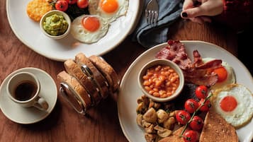 Impostazione per la colazione con piatti di uova, pancetta, fagioli, pane tostato e una tazza di caffè.