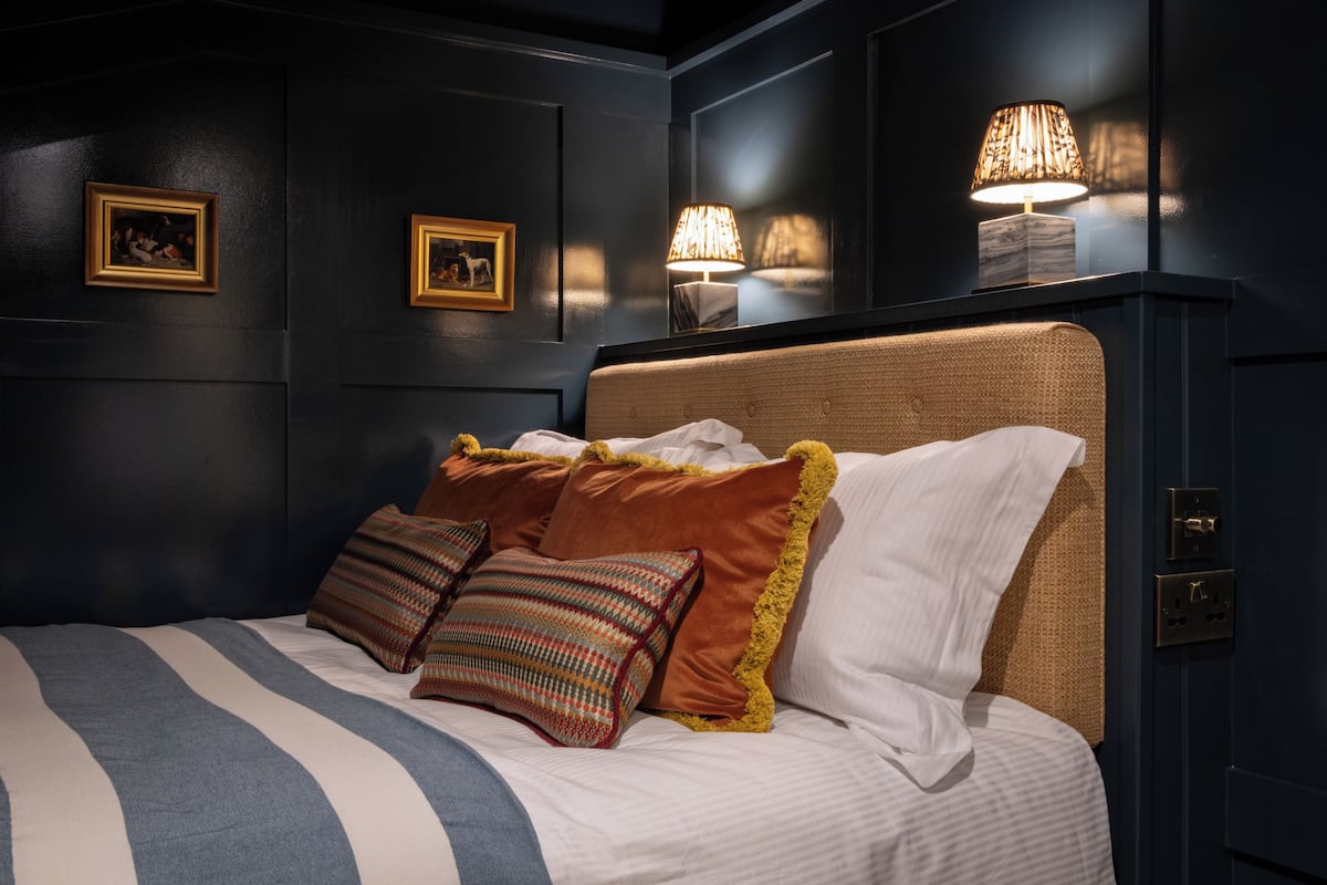 Una cama bien tendida con ropa de cama a rayas, un cabecero tejido y varios cojines decorativos.