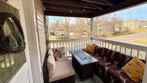 Une véranda abritée avec un coin salon doté de coussins, une petite table et une vue sur un quartier résidentiel.