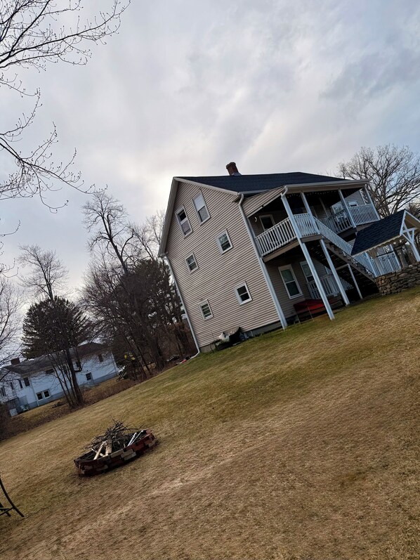 A two-story house with a balcony, a stone foundation, and a grassy yard.
