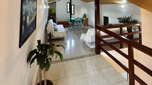 A spacious room with a high ceiling and wooden beams, a dining area with a table and chairs, and a staircase with a wooden railing. - Refuge Brisa do Campo | IG - SOLAR DO CAMPO (Rio de Janeiro)