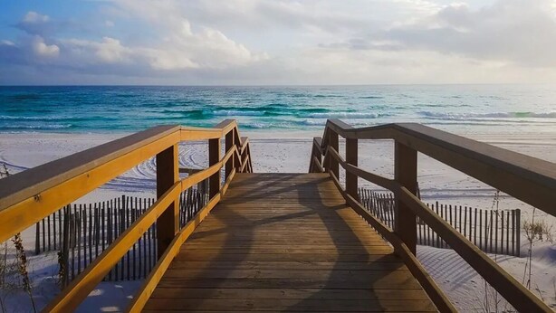 Un paseo marítimo de madera que lleva a una playa con vista despejada al océano.