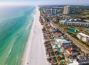Vista aerea di una località balneare con proprietà sulla spiaggia, un grande complesso alberghiero e una zona con piscina.