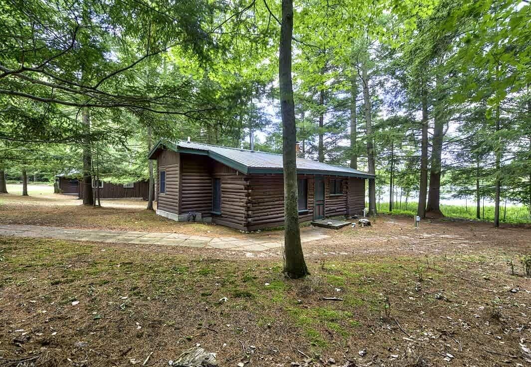 A log cabin with a porch, surrounded by tall trees in a wooded area.