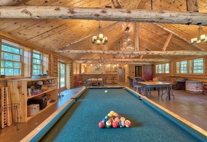 Un amplio espacio interior con piscina, vigas de madera, mesa de billar y varias bolas de billar.