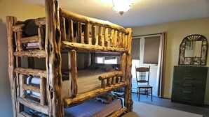 Een rustiek houten stapelbed met een ladder, een stoel, een dressoir en een spiegel in een slaapkamer.