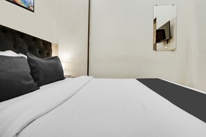 A neatly made bed with white and black bedding, a tufted headboard, and a small mirror on the wall.